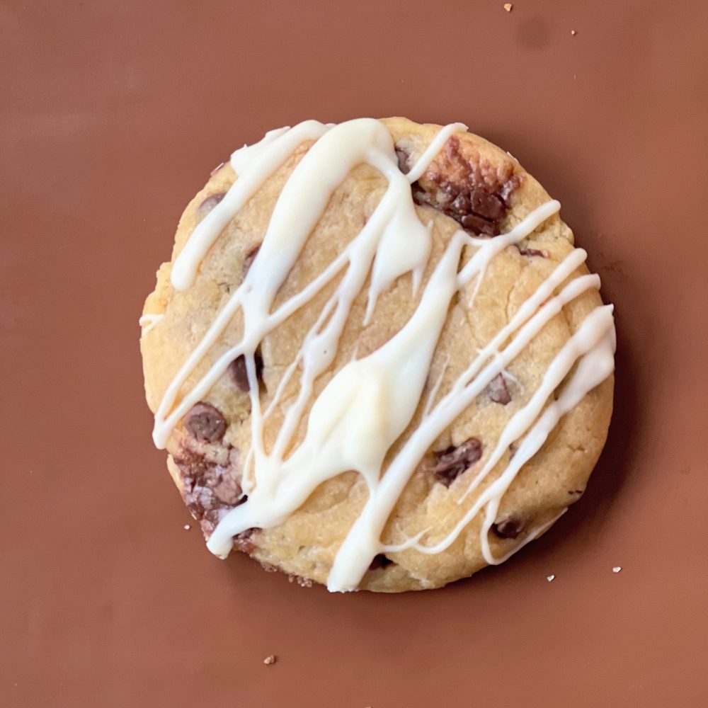 MELT. Hazelnut Choc Chip cookie with white chocolate drizzled across the top, on brown paper